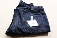 Folded blue denim jeans with a visible back leather waistband patch labeled U.S.A. and a tag number 65 attached to back pocket.