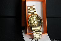 Front view of vintage Seiko watch resting in an orange box, showing its gold-tone metal band and bronze faceted dial.