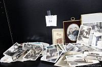 Wide view showing a collection of antique and vintage photographs spread on a surface with framed items at the back, including a framed oval portrait on velvet.