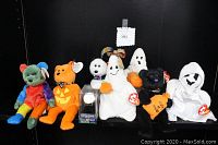 Photo showing seven TY Beanie Babies Halloween themed plush toys arranged side by side with a rotating disc spider watch in its packaging in front.