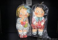 Photo of two vintage Campbell's Kids soft toy dolls, sealed in plastic bags, one blonde with blue bow, one black-haired with striped outfit