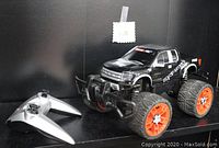Black Carrera RC Ford F-150 Raptor SVT remote control truck with orange wheels and accompanying gray remote control.