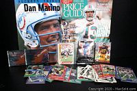Full view of the lot showing the Beckett Dan Marino Tribute magazine, Sports Collectors Digest Price Guide, multiple loose and packaged football trading cards spread around them