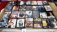 Photo showing 35 assorted DVDs on a table including titles such as 'The Suspect', 'The Firm', 'Salt', 'Any Given Sunday', 'Shattered Glass', 'Julie & Julia', and more.
