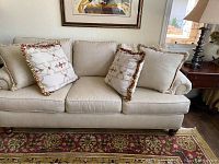 Front view of the three-seat beige upholstered sofa with four decorative throw pillows arranged on the seat cushions