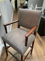 Barstool showing upholstered seat and back, wooden frame, armrests.