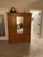 Full front view of the wooden armoire with central mirror door, multiple drawers below, and decorative molding on the top edge.
