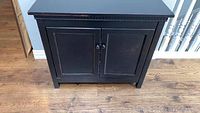 Front view of black distressed Crate and Barrel chest with two doors and round knobs on wooden floor