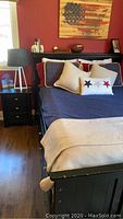 Full view of queen size bed frame with bedding, distressed black finish, headboard visible, nightstand on left.
