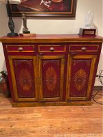 Front view of decorative wooden cabinet with three drawers and carved doors below.