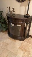 Front view of dark wood curved glass cabinet with drawer and doors