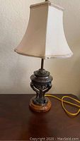 Full view of the decorative lamp with beige fabric shade, dark metal detailed body, and wooden base.