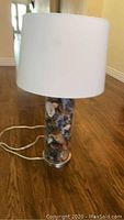 Full view of the lamp showing the white fabric lampshade, glass base filled with potpourri, and power cord.