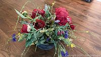 Silk flower arrangement from an overhead view showing red roses and colorful accents on wooden floor.