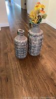 Two clay urns of different sizes placed on wooden floor, decorative basket-weave pattern visible.