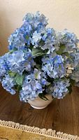 Full artificial blue hydrangea flower arrangement in white ceramic pot approximately 24 inches tall on wood surface.