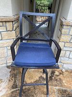 Front view of black metal outdoor bar stool with navy blue cushion, showing X design backrest and armrests.