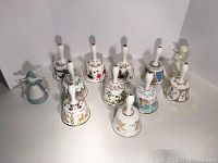 Ten Hammersley annual collector bells with white handles arranged in a group with two white porcelain angels.