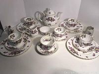 Full tea set including teapot, four teacup, saucer, plate trios, creamer, and sugar bowl arranged on white surface.