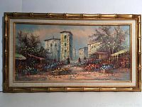 Full view of the framed oil painting showing a village market street scene with tall buildings and colorful flowers.