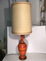 Full view of tall Mid Century Modern lamp with beige fabric shade and orange-brown striped ceramic body.