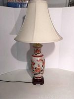 Full view of the lamp showing beige fabric shade and floral porcelain body on wooden base