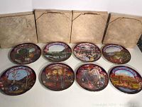 All eight collector plates laid out with four original boxes behind them. Shows detailed painted scenes with ornate borders.