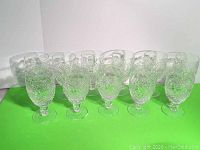 Set of eleven Galway Irish Crystal red wine goblets on a green surface, arranged in a row.