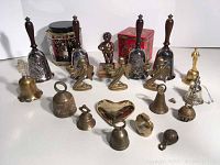 Lot of various bells including four silver plate Norman Rockwell bells with wooden handles, bronze pisser on onyx, brass candle holders, and other assorted brass and metal bells with two decorative tins.