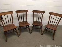 Four Temple Stuart early American style wooden chairs, spindle backs, turned legs, warm finish, arranged in a row.