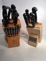 Front view of two wooden blocks with Wolfgang Puck branding each holding a set of kitchen knives with black handles.