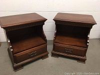Two matching wooden night stands side by side showing front view, dark brown wood finish, one drawer and open shelf each.