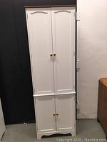 Front view of closed white tall cabinet with four doors and wooden knobs.