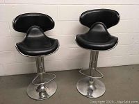 Front view of two black and chrome bar stools with curved seats and backs and round chrome bases.