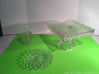 Three items: Fostoria pedestal cake plate, round server plate, covered sugar bowl, displayed on green backdrop.