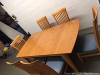 Dining table with six matching chairs in natural light wood and blue padded seats, table in closed position.