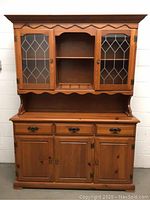 Front view of pine china hutch with two leaded glass doors, open center shelf, three drawers below, and three cabinets at the bottom.