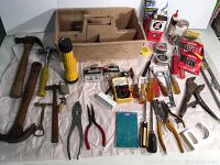 Wide view of assorted hand tools spread out including hammers, screwdrivers, pliers, flashlight, wooden organizer box and small hardware items