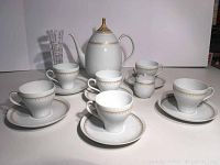 Full view of coffee pot, cups, saucers, sugar bowl with spoon, and glass vase arranged on white surface