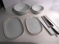 Photo showing all items in the lot: two bowls of different sizes, three rectangular platters, and a cheese shaver on a tray, all with gold trim Poesie pattern.