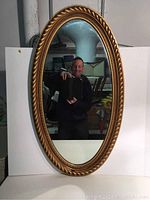 Front view of the oval wall mirror showing its decorative gold-colored frame and reflective surface.