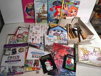 Full overview of assortment showing multiple coloring books, crafting guides, small paintbrushes, and other art items organized on table.