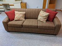 Front view of ROWE Furniture soft brown sleeper sofa with two solid red and two patterned pillows on it.