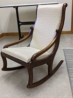 Front angle view of antique rocking chair showing wooden frame and cream upholstery
