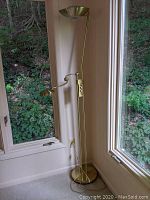 Full view of brass floor lamp standing in corner with two lights, tall and slim design with round base.