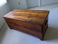 Full angle view of the cedar wood blanket chest showing front and side with metal casters and side handles.