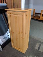 Front view of the small wooden pantry cabinet closed, showing wood grain and door panel.