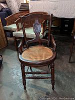 Front view of the vintage solid wood side chair with carved wooden details and caned seat in good condition.