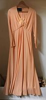 Full view of the peach vintage dress hanging on a hanger showing long sleeves and full length skirt.