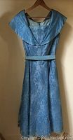 Full view of the vintage blue dress hanging showing wide collar and flared skirt